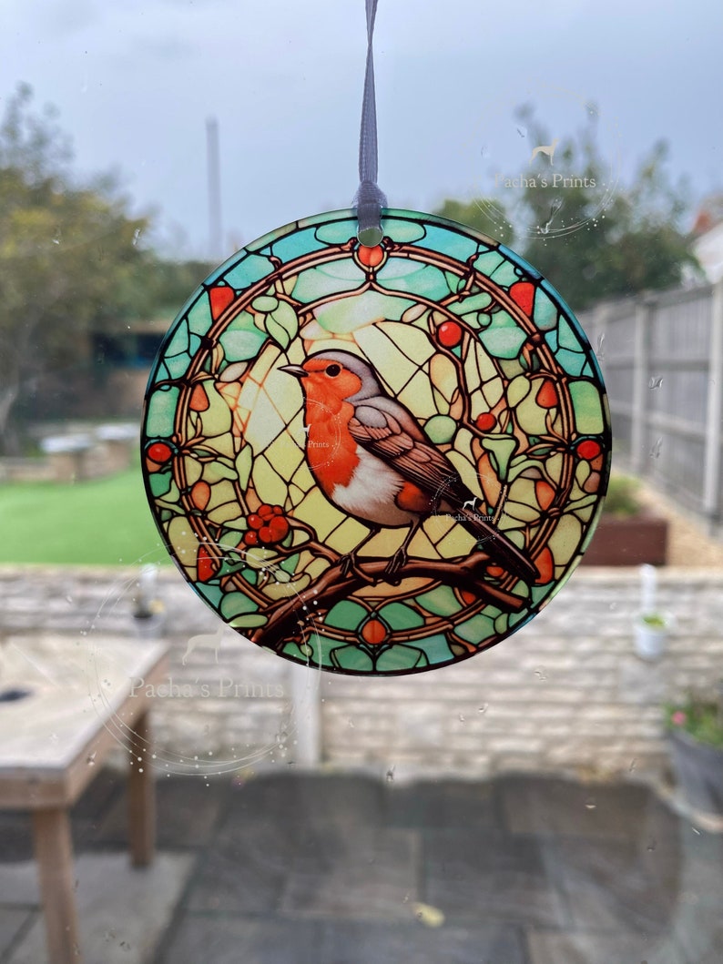 May include: A round stained glass ornament featuring a robin perched on a branch with red berries. The ornament has a blue, green, and yellow stained glass design.