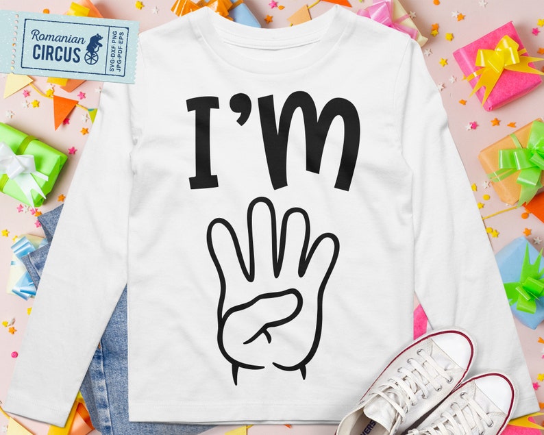 Pu&ograve; includere: Maglietta bianca a maniche lunghe con testo nero che dice "I'm" e un'illustrazione nera di una mano con quattro dita alzate.