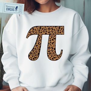 Puede incluir: Sudadera blanca con un gran símbolo Pi con estampado de leopardo marrón y negro. La sudadera tiene cuello redondo y mangas largas. Una pequeña etiqueta con texto es visible en la esquina superior izquierda.