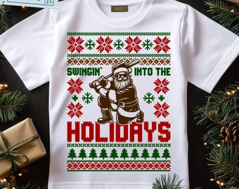 May include: White t-shirt with a festive design. The shirt features a graphic of Santa Claus swinging a baseball bat, with the text "SWINGIN' INTO THE HOLIDAYS" in red and green. The design includes snowflake and Christmas tree patterns.