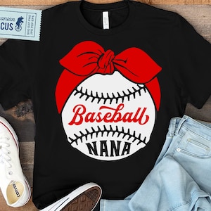 May include: Black t-shirt featuring a white baseball with red stitching and a red bandana on top. The baseball has the text "Baseball Nana" on it.
