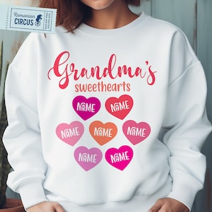 Könnte beinhalten: Weißer Pullover mit dem Text "Grandma's sweethearts" in rosa und roten Buchstaben. Es gibt sechs rosa, rote und orangefarbene Herzen mit dem Wort "NAME" in weiß in jedem Herzen.
