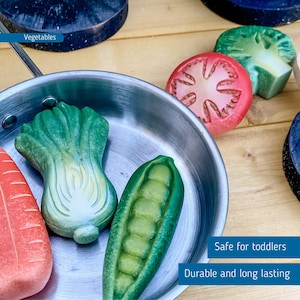 May include: A silver toy pan filled with wooden toy vegetables, including a green pea pod, a green lettuce, and a red carrot. The text "Vegetables" is visible in the top left corner of the image. The text "Safe for toddlers" and "Durable and long lasting" is visible in the bottom right corner of the image.