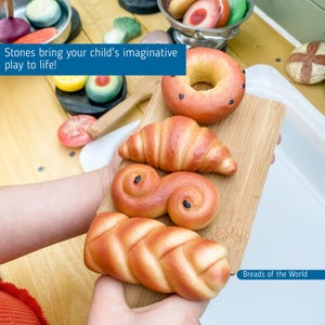 May include: A set of four different types of breads, including a croissant, a cinnamon roll, a braided loaf, and a donut. The breads are all made of dough and are a light brown color. The breads are arranged on a wooden cutting board. The text "Breads of the World" is visible in the bottom right corner of the image.