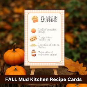 May include: A recipe card on a small easel with the text "PUMPKIN MUFFINS" and instructions. The card is decorated with illustrations of ingredients and a pumpkin. Two pumpkins sit in front of the card. The text "FALL Mud Kitchen Recipe Cards" is at the bottom.