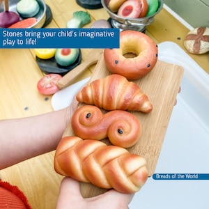 May include: A set of four different types of breads, including a croissant, a cinnamon roll, a braided loaf, and a donut. The breads are all made of dough and are a light brown colour. The breads are arranged on a wooden chopping board. The text "Breads of the World" is visible in the bottom right corner of the image.