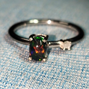 May include: A silver ring with a black opal gemstone and a small diamond accent.