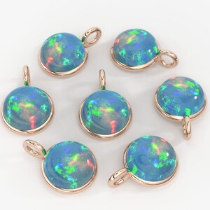 May include: Six round pendants featuring cabochon-cut blue opals with vibrant green and red flashes, each set in a polished rose gold-toned metal bezel with a small circular bail attached at the top for hanging on a chain or cord.