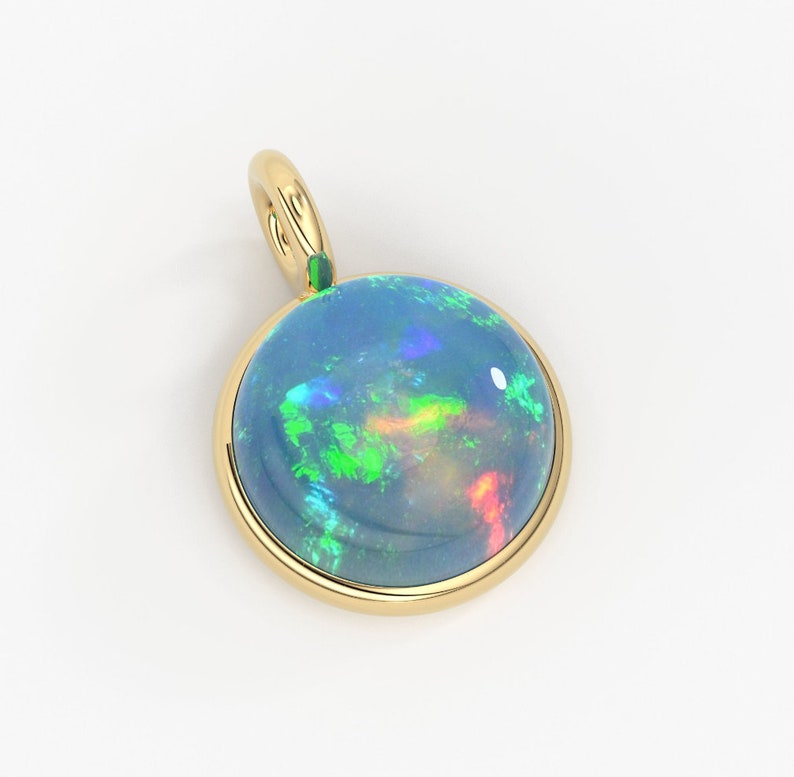 May include: A round pendant featuring a polished cabochon opal set in a smooth yellow gold bezel. The opal displays a dark blue base color with vibrant flashes of green, red, and blue light. A small gold bail is attached to the top of the setting.