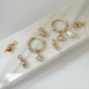 May include: Gold hoop earrings with various charms, including a seashell, starfish, fish, seahorse, and a pearl. The charms are attached to the hoops with jump rings.