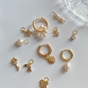 K&ouml;nnte beinhalten: Eine Sammlung goldener Creolen mit verschiedenen Anh&auml;ngern, darunter eine Perle, ein Stern, ein Schmetterling, eine Sonne, ein Regenbogen, ein Schl&uuml;ssel, eine Wolke und ein Quadrat. Die Anh&auml;nger sind aus Gold und haben kleine Kristalle oder Perlen.
