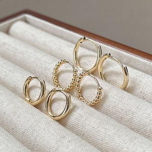 Peut inclure: Ensemble de quatre boucles d'oreilles créoles dorées, deux lisses et deux avec un design perlé.