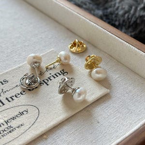 May include: Four pearl pins with gold and silver clasps. The pins are displayed on a white fabric surface with the text "Old tree spring" and "n jewelry box to meet you".