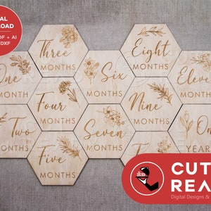 May include: Twelve wooden hexagonal baby milestone markers with floral designs and the text "One Month", "Two Months", "Three Months", "Four Months", "Five Months", "Six Months", "Seven Months", "Eight Months", "Nine Months", "Eleven Months", "One Year".