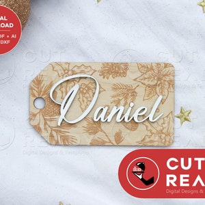 Puede incluir: Una etiqueta de regalo de madera marrón con un diseño floral y el nombre "Daniel" en letras blancas. La etiqueta es perfecta para un regalo de Navidad.