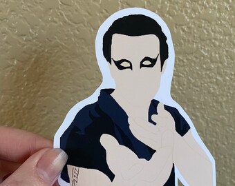 Peut inclure: Un autocollant noir et blanc d'une personne avec des cheveux noirs et une chemise noire. La personne a un eye-liner noir et un tatouage sur le bras.