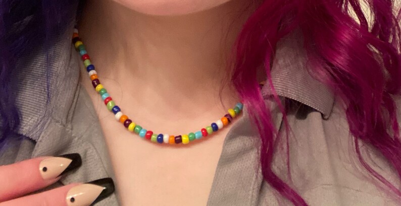May include: A colorful beaded necklace with a variety of colors, including red, orange, yellow, green, blue, purple, and white.
