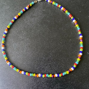 May include: A colorful beaded necklace with a variety of colors including red, orange, yellow, green, blue, purple, and white.
