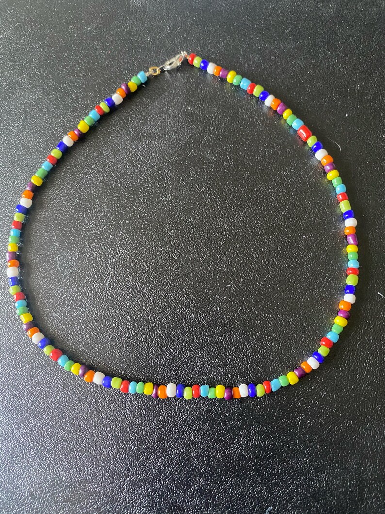 May include: A colorful beaded necklace with a variety of colors including red, orange, yellow, green, blue, purple, and white.