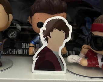 May include: A white sticker featuring a silhouette of a person with brown hair and a maroon shirt. The person is facing the right side of the image.