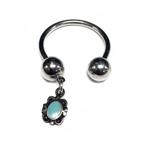May include: Silver horseshoe shaped ring with a small turquoise charm hanging from the bottom.