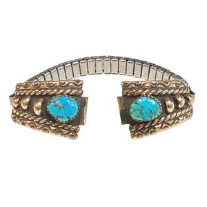 May include: Vintage turquoise cuff bracelet with a silver and gold-tone metal band. The bracelet features two oval turquoise stones set in decorative gold-tone metal. The band is a silver-tone, expandable style.