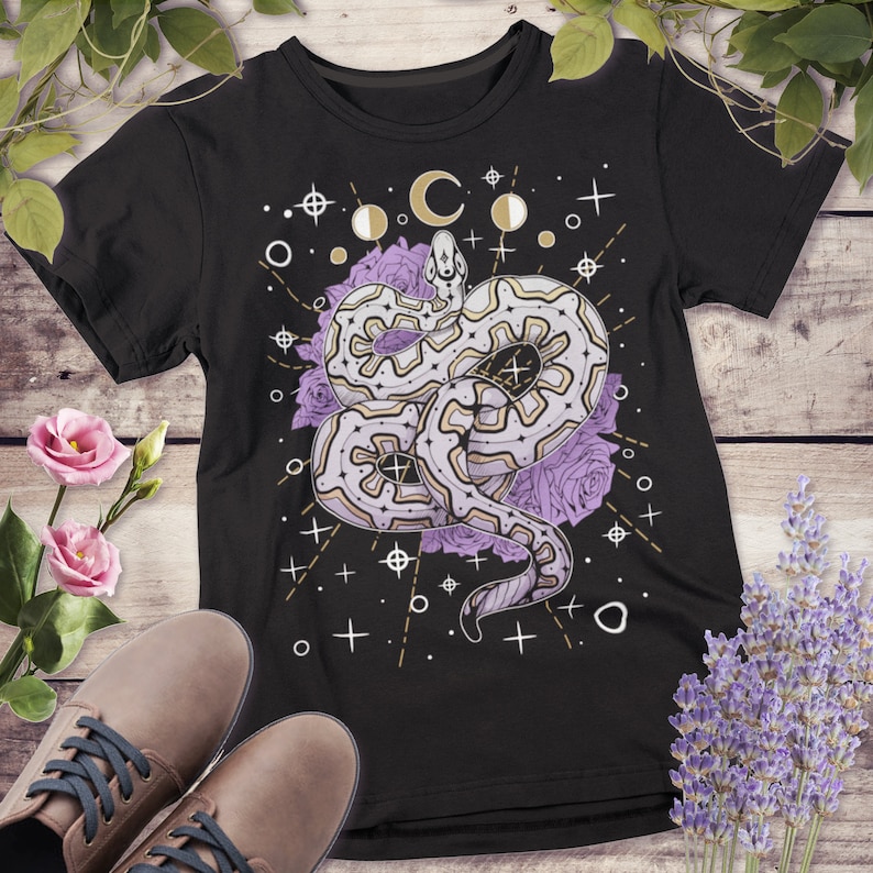 May include: Black t-shirt featuring a graphic of a white snake with a geometric pattern, surrounded by purple roses and gold stars and moons.