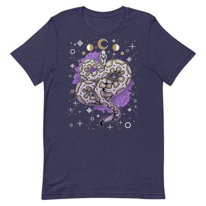 May include: A navy blue t-shirt featuring a white and gold design of a snake with purple flowers and celestial symbols.