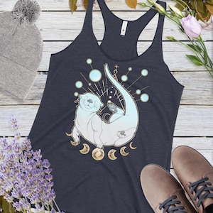 May include: A navy blue tank top with a white and blue illustration of an otter swimming in a circle of moons. The otter is surrounded by a celestial design with stars and dots.