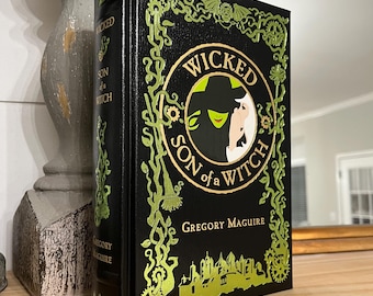 May include: A black leather-bound book with gold lettering and illustrations. The title is "Wicked: Son of a Witch" by Gregory Maguire.