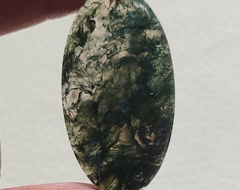 May include: An oval-shaped moss agate gemstone. The stone features a translucent base with intricate patterns of green, brown, and white inclusions, resembling a miniature landscape. The polished surface reflects light, highlighting the natural beauty of the stone.