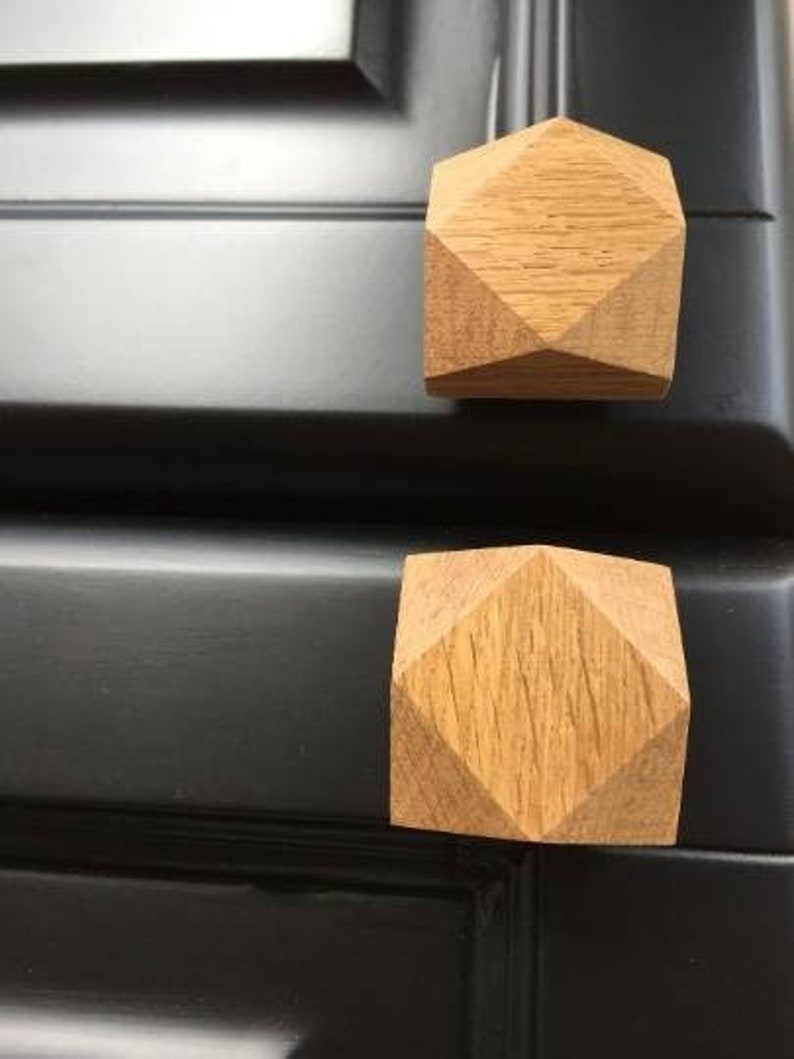 以下が含まれることがあります： ダイヤモンド型の幾何学模様が施された木製のキャビネットノブ2個。ノブは薄い茶色の木でできており、黒い表面に取り付けられています。