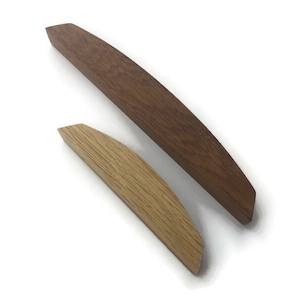 May include: Two wooden cabinet pulls, one is a light brown wood and the other is a darker brown wood. Both pulls are curved and have a rounded edge.