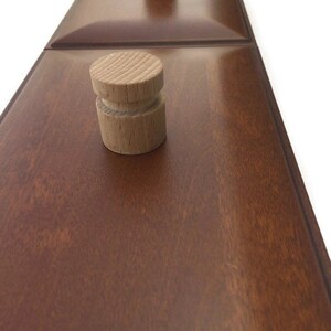 May include: Two wooden knobs with a rounded top and a cylindrical base are mounted on a dark brown wooden surface.