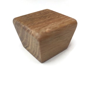 Könnte beinhalten: Ein quadratischer, brauner Holzknauf für einen Schrank. Der Knauf hat eine leicht abgerundete Oberseite und eine glatte Oberfläche.