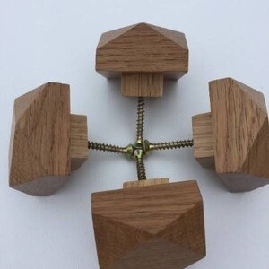 以下が含まれることがあります： 幾何学模様のついた木製のノブが4つ。ノブは金属製のネジでつながっています。ノブは薄い茶色です。