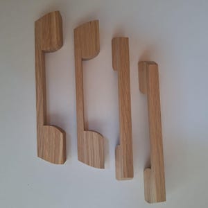 Könnte beinhalten: Vier Holzknaufgriffe in verschiedenen Größen. Die Griffe sind alle aus hellem braunem Holz und haben ein schlichtes, modernes Design.