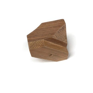 Puede incluir: Una peque&ntilde;a forma geom&eacute;trica de madera de color marr&oacute;n claro. La forma tiene un agujero en el centro.