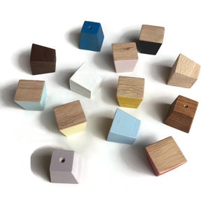 Op de afbeelding: Een verzameling van 13 geometrische houten haken in verschillende kleuren, waaronder blauw, bruin, wit, geel, roze en lichtblauw. Elke haak heeft een klein gaatje bovenaan om items aan op te hangen.