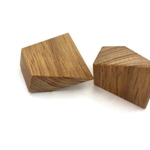 Op de afbeelding: Twee driehoekige houten blokken, een ligt op zijn zijde en de andere staat rechtop. Beide blokken hebben een natuurlijke houten afwerking en een nerfpatroon.