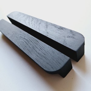 Op de afbeelding: Twee zwarte houten telefoonstandaards met afgeronde randen. De standaards zijn gemaakt van donker hout en hebben een gladde afwerking.