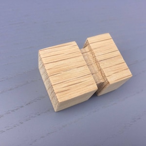 May include: Two wooden blocks joined together, one block is slightly larger than the other. The blocks are made of light wood with a natural grain pattern.