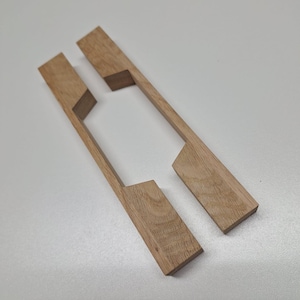 May include: Two wooden, light brown, rectangular pieces with a cutout design. The pieces are positioned parallel to each other, suggesting they are components of a larger item. The wood grain is visible.