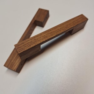 May include: Two wooden cabinet pulls with a rectangular shape and a cut-out handle. The pulls are made of a dark brown wood.