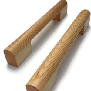Könnte beinhalten: Zwei Holzknaufgriffe für Schranktüren mit abgerundeter Oberseite und rechteckigem Sockel. Die Griffe sind aus hellem braunem Holz mit sichtbarer Maserung.