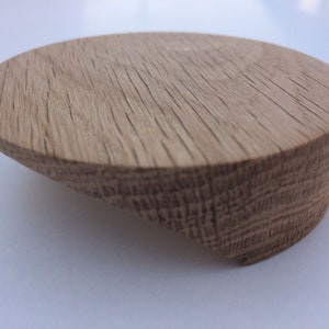 Könnte beinhalten: Ein runder Holz-Knopf mit hellbrauner Oberfläche. Der Knopf hat eine geschwungene Form und eine glatte Oberfläche.
