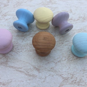 Może przedstawiać: Sześć drewnianych gałek w różnych pastelowych kolorach, w tym jasnoniebieski, żółty, lawendowy, różowy i brązowy. Gałki są ułożone w półkole na jasnoszarym tle.