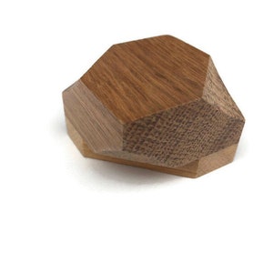Könnte beinhalten: Eine geometrische Holzkiste mit sechseckiger Form. Die Kiste besteht aus zwei Holzstücken, einem hellbraunen und einem dunkleren braunen. Die Kiste ist geschlossen und liegt auf der Seite.
