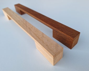 Könnte beinhalten: Zwei Holzknaufgriffe, einer aus naturbelassenem Holz und einer in einem dunklen Braun gebeizt. Beide Griffe haben eine rechteckige Form mit einem Ausschnitt in der Mitte.