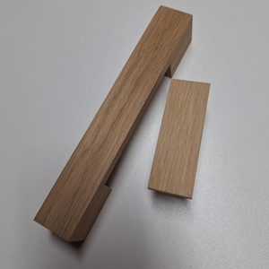 Op de afbeelding: Twee houten deurknoppen voor kasten, een lange en een korte, met een rechthoekige vorm en een gladde, natuurlijke houten afwerking.